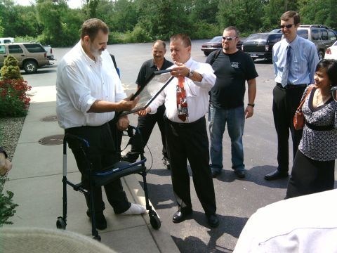 1985 Ford LTD Crown Victoria - A group of people gather outdoors as one man presents a framed item to another.