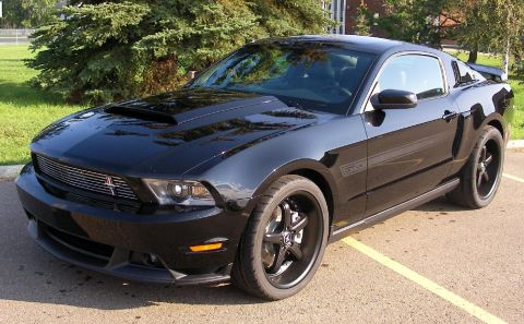 2008 Ford Mustang - Black Ford Mustang with racing stripes and aftermarket wheels parked outside.