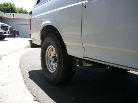 1988 Ford Bronco - A white 1988 Ford Bronco is seen from the side, dual exhaust pipes and a camper shell.