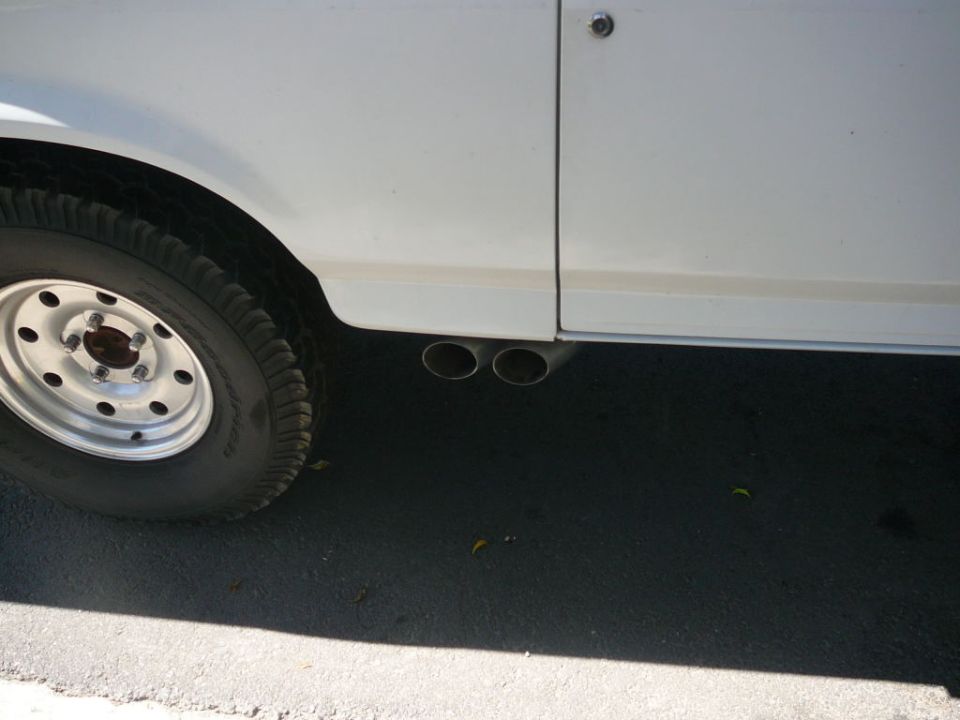 Close-up of dual exhaust pipes exiting under the side of a white vehicle near the rear wheel