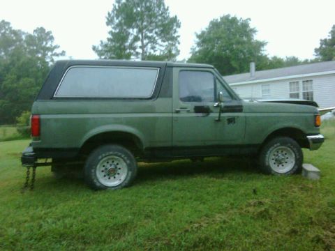 1990 Ford Bronco - A green 1990 Ford Bronco is shown from the side with its hood open, parked on a grassy area.
