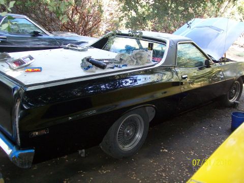 1972 Ford Ranchero - A black 1972 Ford Ranchero is parked outside with its hood open and various parts laid out on the bed cover.