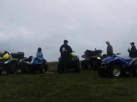 2000 Ford E350 - People gathered with multiple ATVs on a grassy incline under an overcast sky.