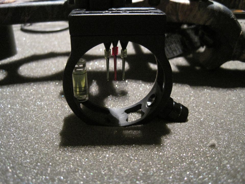 Close-up of a black archery bow sight with a bubble level and three pins (two red, one silver)
