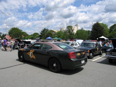1991 Ford LTD Crown Victoria - Rear three-quarter view of a dark green Dodge Charger state police car parked in a row of cruisers at an outdoor car show.