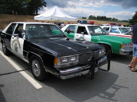 1991 Ford LTD Crown Victoria - Front view of a black and white Ford highway patrol car with brush guard, lined up with a green cruiser at an outdoor show.