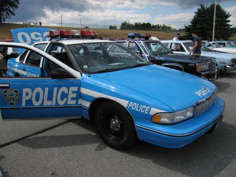 1991 Ford LTD Crown Victoria - blue Chevrolet Caprice police car marked POLICE with its door open, parked in a row of cruisers at an outdoor car show.