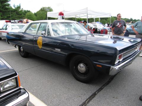 1991 Ford LTD Crown Victoria - dark blue Plymouth police sedan with a gold door emblem and single roof light, parked at an outdoor car show with onlookers.
