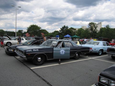 1991 Ford LTD Crown Victoria - two-tone State Police sedan with its driver door open and a round emblem on the door is displayed in a cloudy parking lot.
