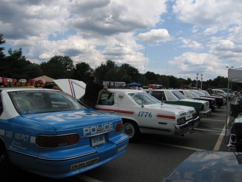 1991 Ford LTD Crown Victoria - row of marked police cars, including a blue #135 sedan reading POLICE and a white #1776 unit, lined up at an outdoor show.