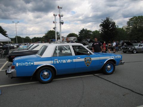1991 Ford LTD Crown Victoria - blue-and-white police sedan marked POLICE and HWY 3 with a city patch and roof light bar is shown in side profile at a car show.
