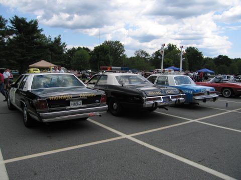 1991 Ford LTD Crown Victoria - Three marked patrol cars seen from behind, including black-and-white HIGHWAY PATROL cars and a blue POLICE unit, lined up at an outdoor sho…