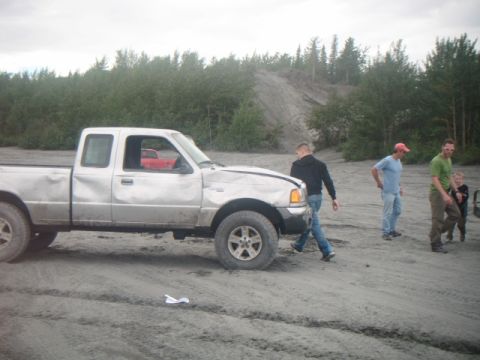 1993 Suzuki Sidekick - A damaged silver pickup truck is parked on a dirt lot with several people nearby.