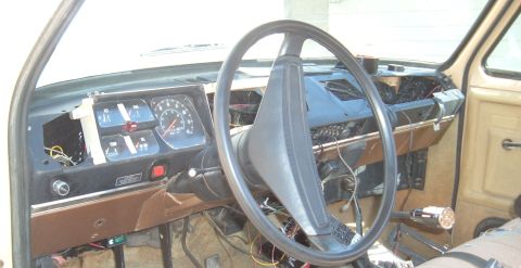 2006 Ford E350 - Torn-apart interior of an older brown-and-blue van dash, viewed from the driver's door across a large two-spoke black steering wheel. The i…