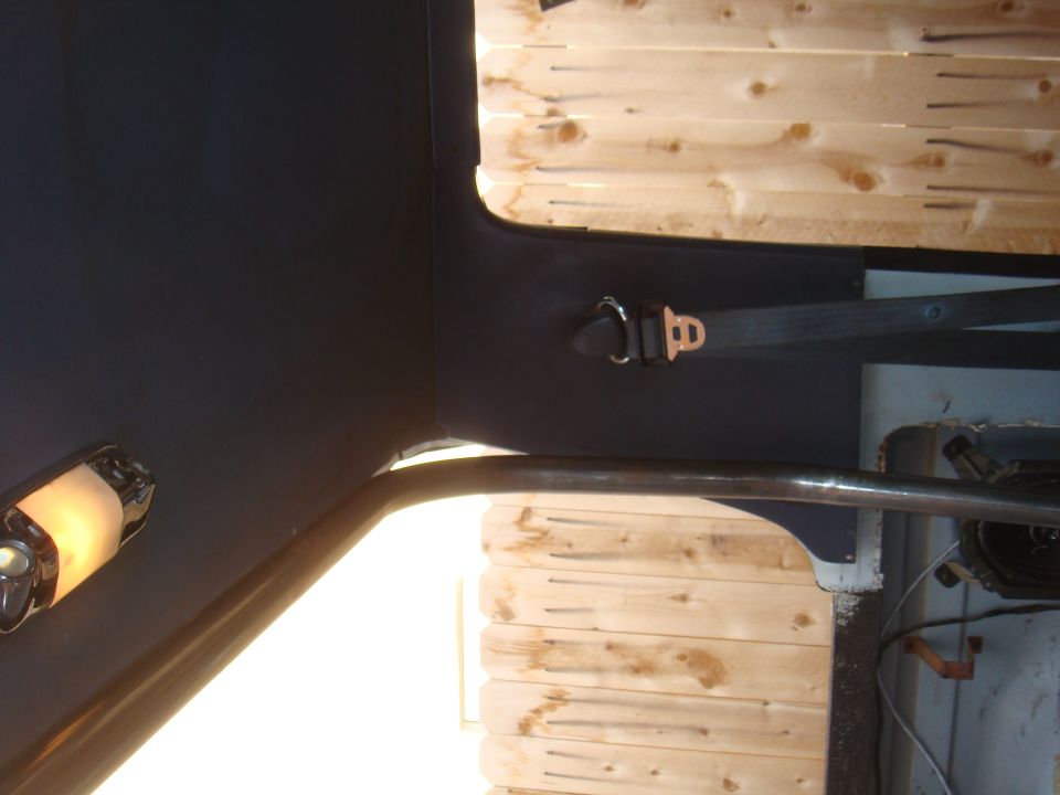 Interior view of a vehicle showing a seatbelt and roll cage against a wood-paneled background