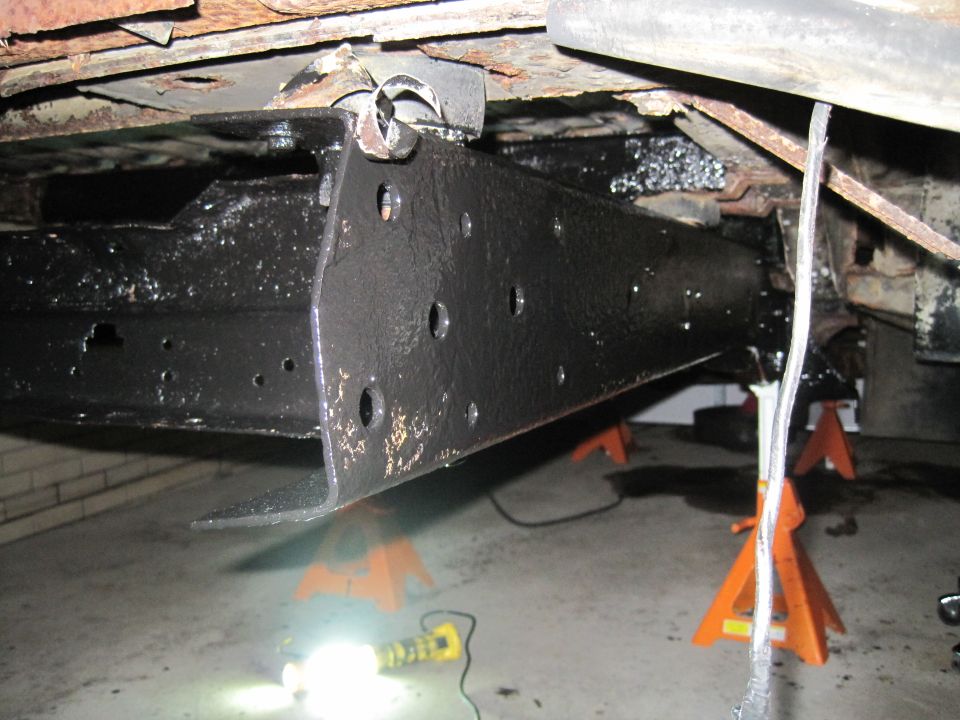 Vehicle frame and suspension parts on jack stands, with black undercoating and rust visible