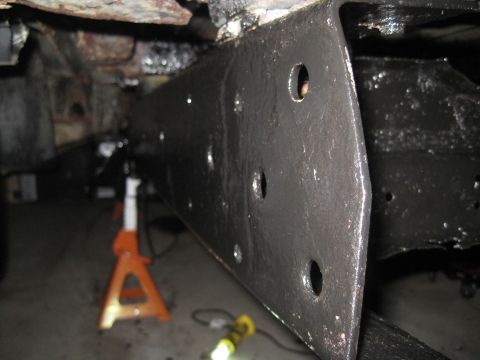 1979 Ford Bronco - Close-up view of a vehicle's frame rail, painted black and several circular holes, resting on orange jack stands.