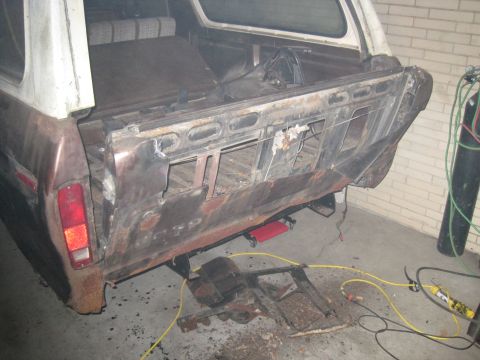 1979 Ford Bronco - The rear of a 1979 Ford Bronco is shown with extensive rust and damage, indicating it is undergoing repairs or restoration.