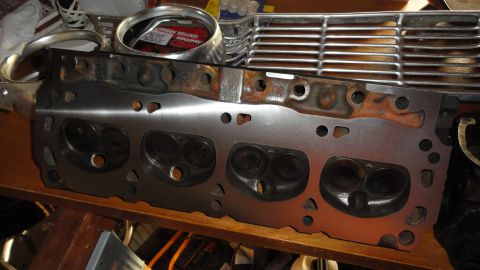 1964 Ford Fairlane - A disassembled engine cylinder head sits on a shelf with other automotive parts, including a chrome grille.