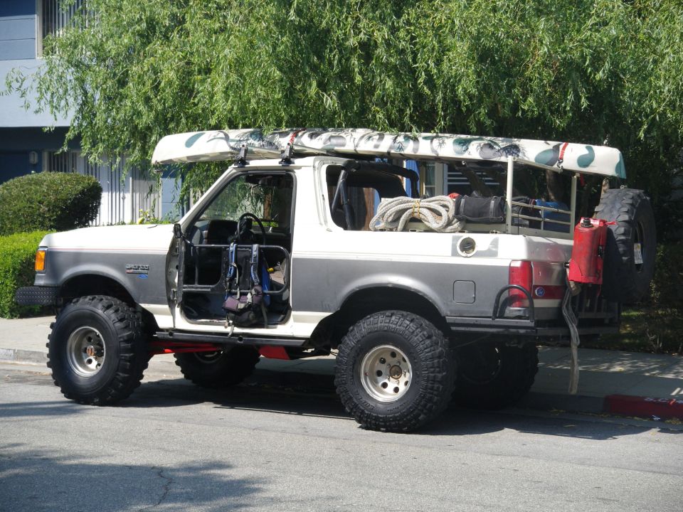 1991 Ford Bronco with doors off, canoe on roof, and spare tire mounted on back