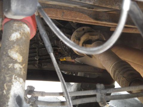 1991 Ford Bronco - Close-up of the undercarriage reveals the complex drivetrain of a vehicle, including the driveshaft and exhaust system.