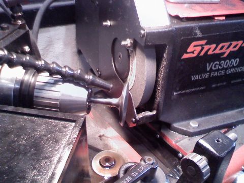 1979 Ford Bronco - An engine valve chucked in a Snap-on VG3000 valve face grinder, with the freshly cut valve face against the grinding wheel and a flexible c…