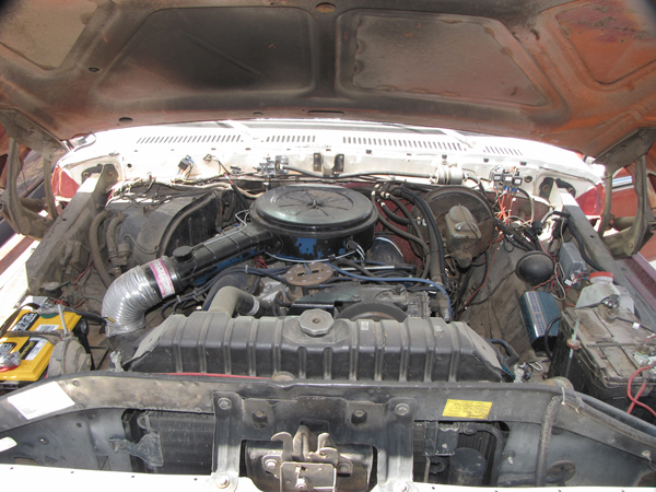 Open engine bay of a red and white vehicle showing V8 engine with black air cleaner and flexible intake duct