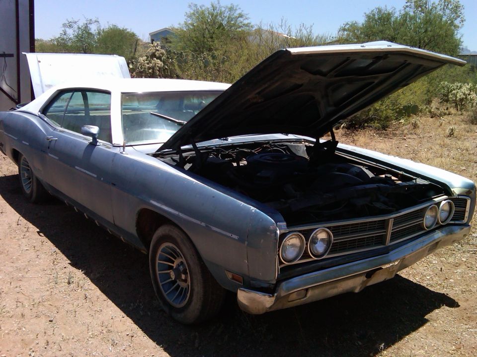 Light blue 2-door coupe with white roof and hood open in a desert dirt lot