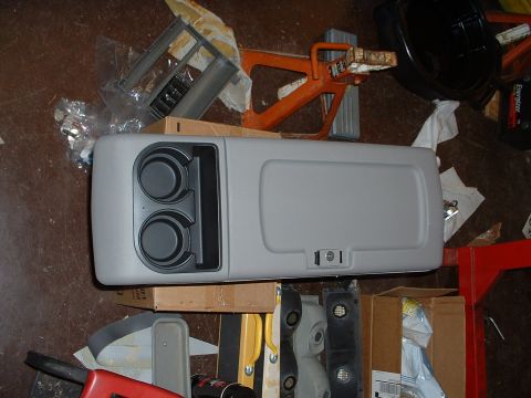 1994 GMC Suburban - A gray center console with cup holders and a storage compartment is shown among various automotive parts.