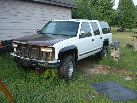 1994 GMC Suburban - This white SUV is parked outside next to a building, with its front end disassembled.