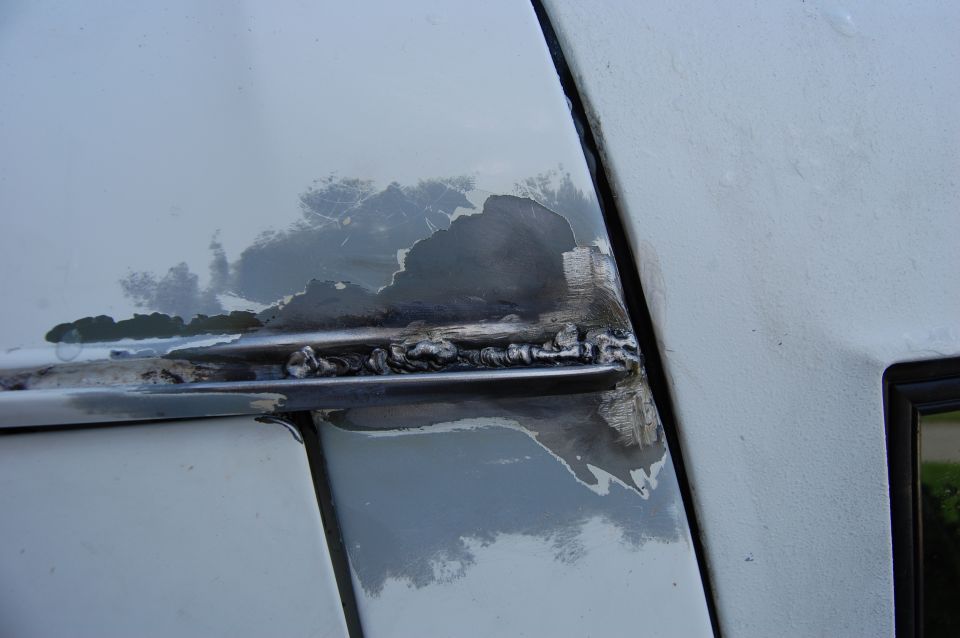 Close-up of rust and peeling paint on a vehicle's body panel, with visible weld marks
