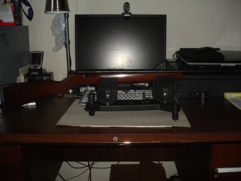 1989 Ford Bronco - A rifle is displayed on a stand on a desk, with a computer and other office items in the background.