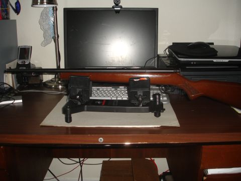 1989 Ford Bronco - A rifle rests on a stand, positioned before a computer monitor and keyboard on a wooden desk.