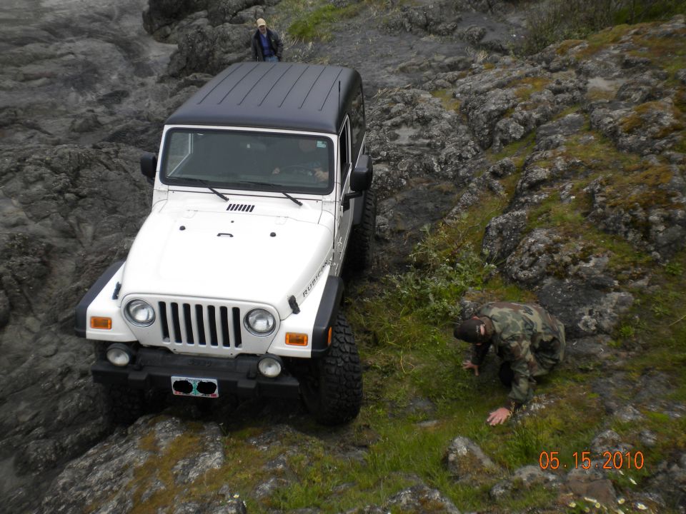 White 2005 Jeep Wrangler with a black hardtop driving on a rocky terrain