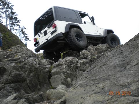 2005 Jeep Wrangler - A white 2005 Jeep Wrangler is shown off-roading over large rocks near a coastline.