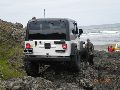 2005 Jeep Wrangler - A white 2005 Jeep Wrangler navigates rocky terrain near the coast, with another vehicle visible in the background.