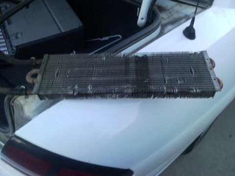 1989 Ford Bronco - A damaged radiator part is shown removed from the trunk of a white vehicle.