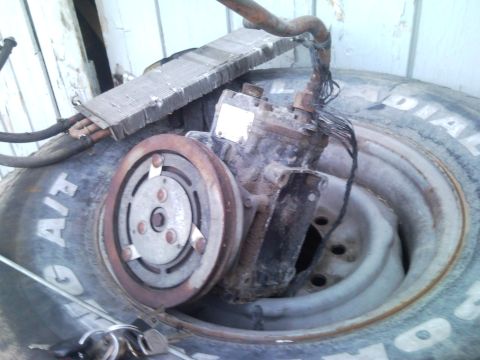 1989 Ford Bronco - Car AC compressor and condenser assembly resting on a tire.