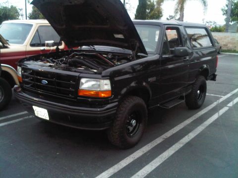 1986 Ford Bronco - Black Ford Bronco parked in a lot with its hood open, next to another vehicle.