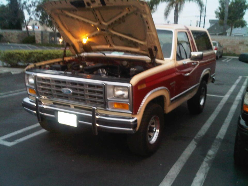 Red and tan Ford Bronco with hood open, parked in a lot