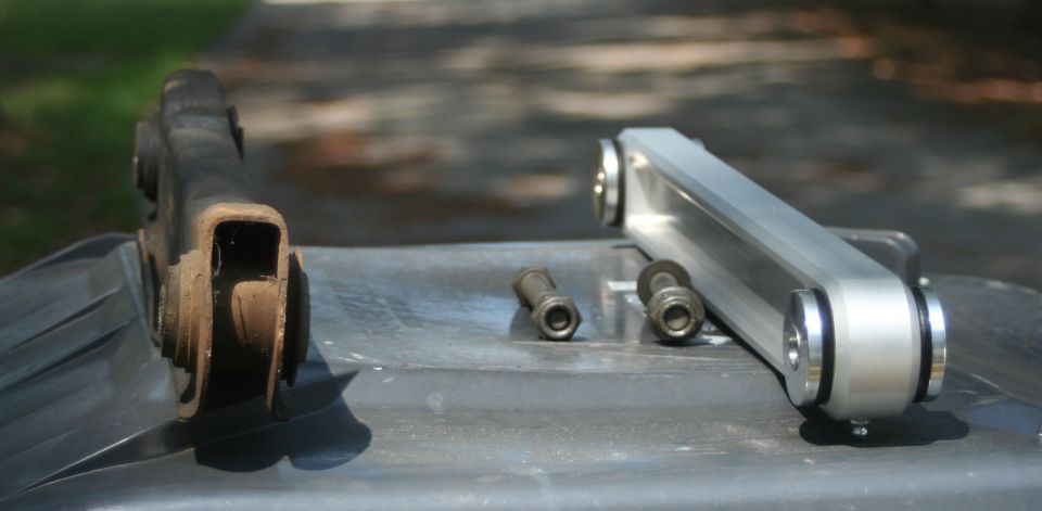 Old rusty and new shiny suspension control arms with bolts on a dark surface
