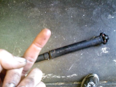 1990 Ford Bronco - A driveshaft is shown, with a finger pointing towards it, suggesting a repair or inspection.