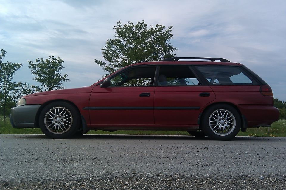 Red 1998 Subaru Legacy station wagon parked on the side of a road, viewed from the side