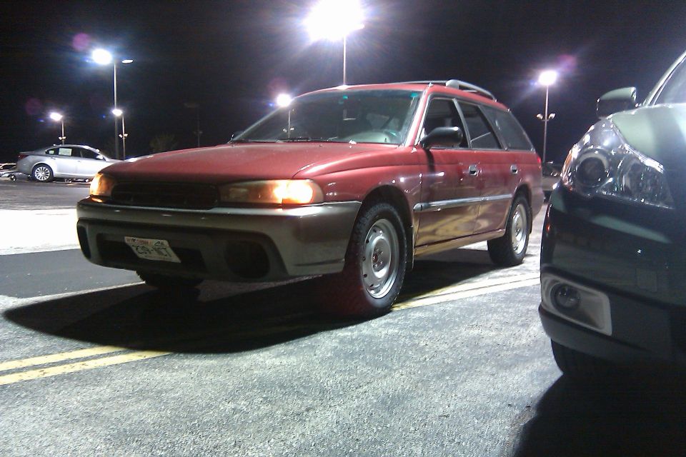 Red 1998 Subaru Legacy wagon, 3q front view, parked at night