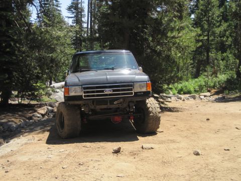 1989 Ford Bronco - This modified Ford Bronco is parked off-road, surrounded by trees and rocky terrain.