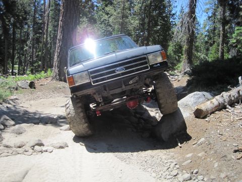1989 Ford Bronco - A black Ford Bronco navigates a rocky trail in a forest setting.