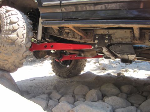 1989 Ford Bronco - The undercarriage of an off-road vehicle features prominent red suspension components and large tires, navigating rocky terrain.