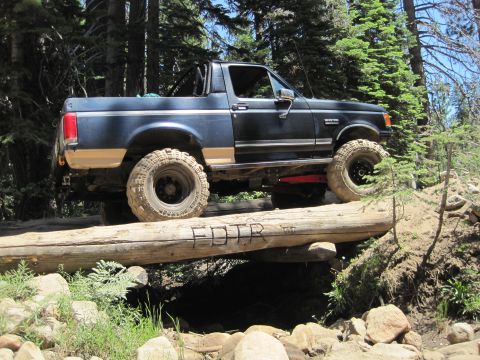 1989 Ford Bronco - This modified Ford Bronco navigates a rough trail, crossing over a large fallen log.