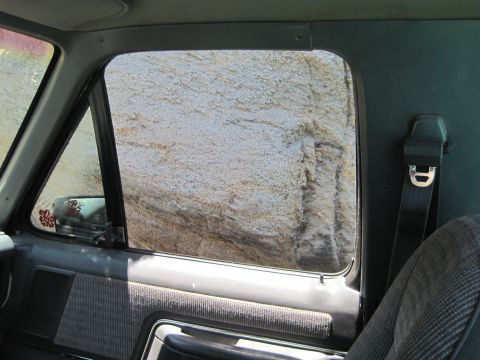 1989 Ford Bronco - The interior of an older vehicle shows a grey patterned seat and door panel, with a rocky landscape visible through the window.