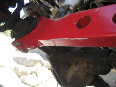 1989 Ford Bronco - The underside of an off-road vehicle shows a red suspension arm and differential, with rocky terrain visible in the background.